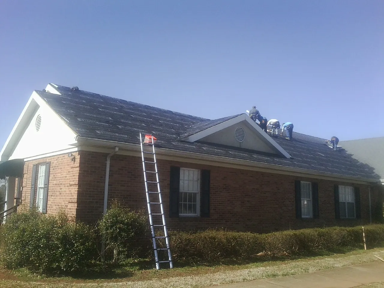Crew tearing shingles off a brick ranch roof with a ladder set — Emergency Roof Repair work by our crew in Harpster