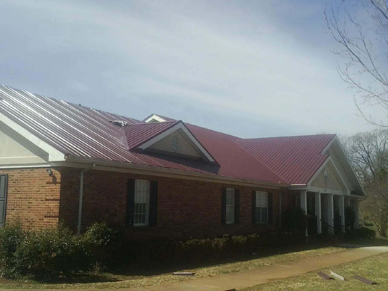 Red metal roof with gabled entries on a long brick building, from a Hail Damage Roof Repair job in Harpster