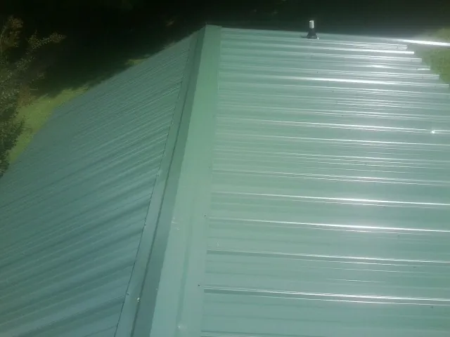 New green metal panels meeting at the ridge of a roof — Flat Roof Repair work by our crew in Harpster