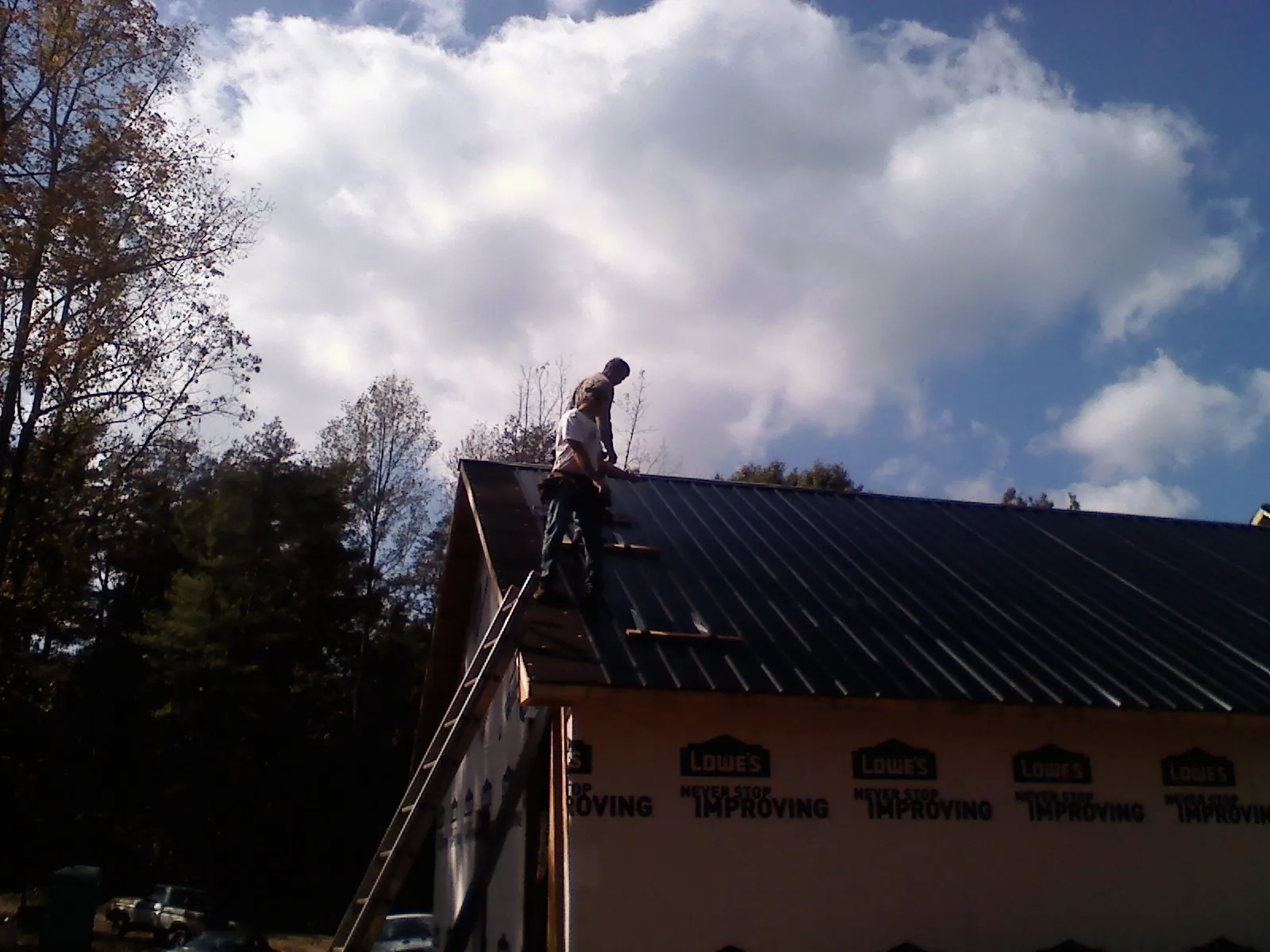 Roofer fastening dark metal panels high against a cloudy sky, from a Roof Inspection job in Harpster