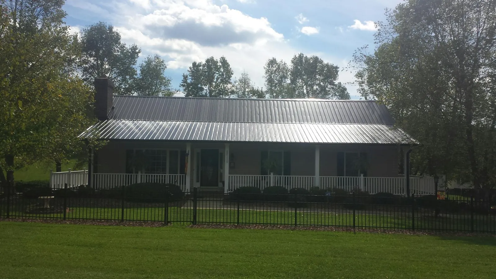 Gray metal roof on a brick ranch with a full width front porch — Gutter Guard Installation work by our crew in Harpster