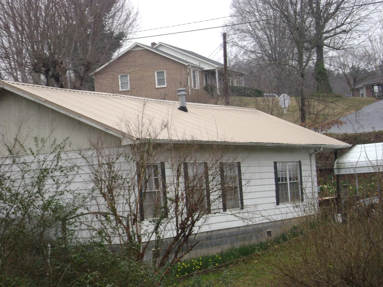 Tan metal roof on a white sided house set into a hillside — Commercial Roofing by Roofing Brothers in Harpster