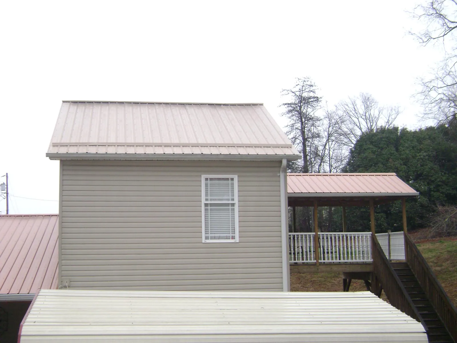 Tan metal roofs on a two story addition and attached porch, from a Roof Replacement job in Harpster